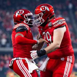 Alex Harrison facing a teammate as they bump helmets on the football field.